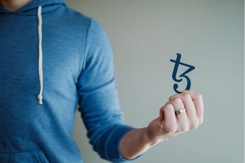 a man in blue hoodie is holding a Tezos logo